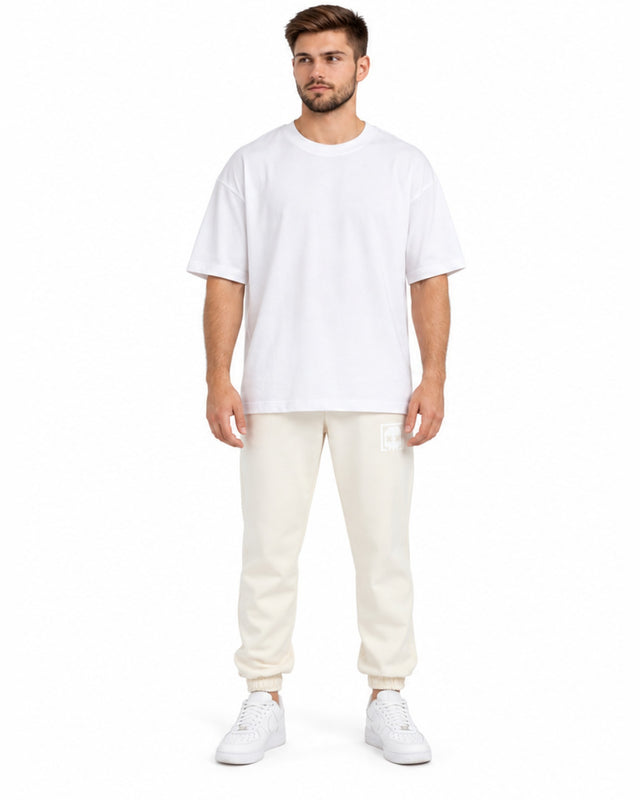 Light-colored jogger pants with elastic cuffs, paired with a loose-fitting white t-shirt and white sneakers.