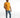 A man stands confidently in a fitted orange shirt and distressed blue jeans, paired with white sneakers.