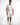 A man wearing a fitted white t-shirt and distressed white shorts with colorful paint splatters, paired with white sne...