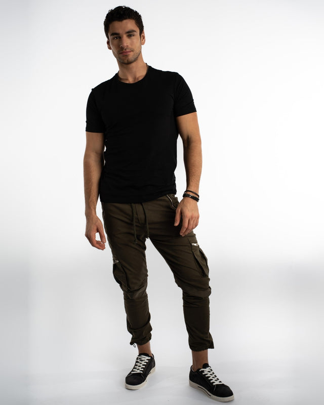 A man stands confidently in a fitted black t-shirt and olive cargo pants, paired with stylish sneakers.