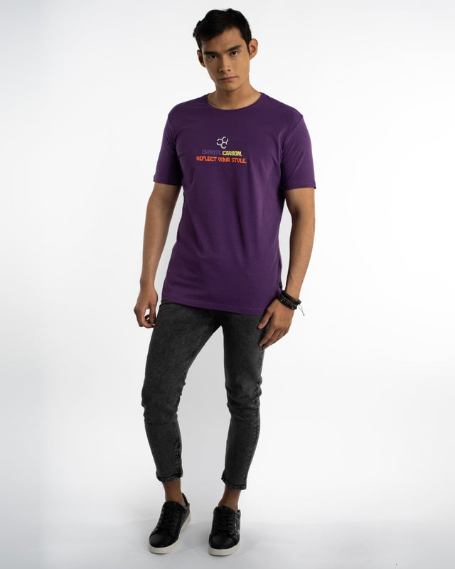 A model stands wearing a purple t-shirt with a graphic design, paired with dark jeans and black sneakers.