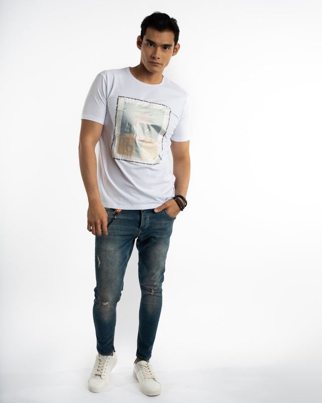 A young man stands confidently in a white t-shirt with a graphic print, paired with distressed blue jeans and white s...