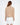 Back view of Serena Serena beige cable knit sweater with a high turtleneck and paired with white skirt.