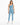 A woman stands confidently in a light blue one-shoulder bodysuit paired with matching leggings and white sneakers.