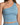 A woman is wearing a light blue, one-shoulder crop top with a fitted design and smooth fabric.