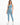 A model poses in a light blue one-shoulder crop top paired with matching high-waisted leggings and white sneakers.