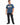 A man stands wearing a blue graphic t-shirt featuring colorful designs and text, paired with black jeans and sneakers.