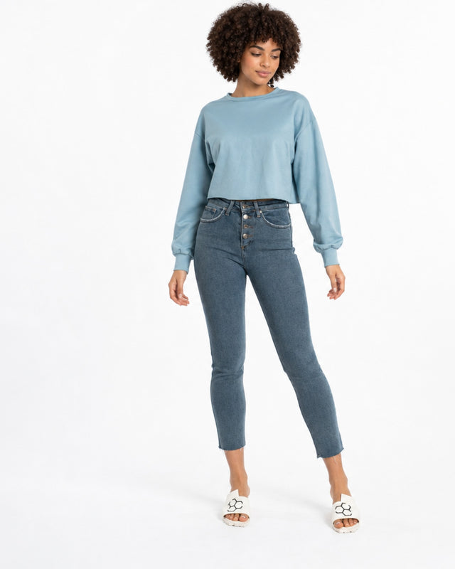 A model wearing a light blue cropped sweatshirt and fitted dark jeans, paired with white slide sandals.
