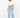 A person stands confidently in a cropped white shirt and light blue wide-leg jeans, paired with sleek black heels.
