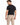 A man stands with his back to the camera, wearing a black t-shirt and beige evening pants with a chain detail.