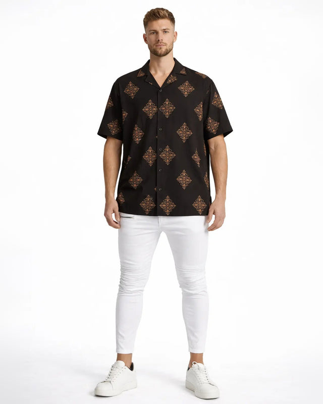 A man stands confidently in a short-sleeve black shirt featuring a colorful diamond pattern, paired with white pants...