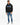 A man stands wearing a black hoodie with blue accents, paired with light blue jeans and stylish sneakers.