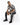 A man sits on a white cube, wearing a black and white patterned short-sleeve shirt with distressed jeans and black sn...