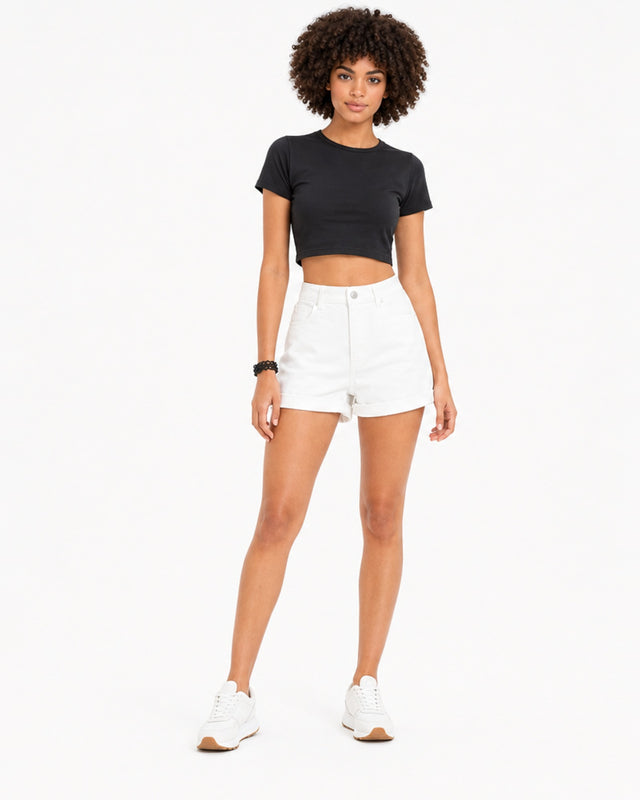 A model poses in a black cropped top and white high-waisted shorts, paired with white sneakers.
