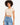 A young woman with curly hair wears a fitted beige crop top paired with high-waisted distressed blue jeans.
