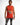 A man wearing a sleeveless bright orange top with graphic text and images, paired with distressed gray jeans.