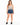 A woman stands confidently in denim shorts paired with a tie-dye tank top and black sneakers.