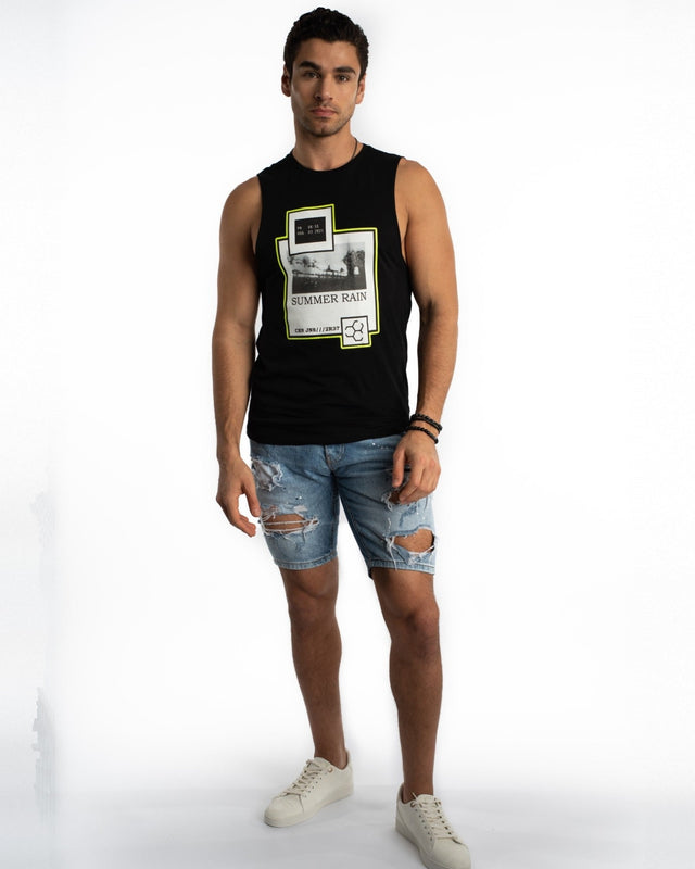 A young man poses in a black sleeveless shirt and distressed denim shorts, paired with white sneakers.