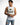 A man wearing a sleeveless white top with a graphic print and distressed denim shorts, posing thoughtfully.