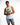 A young man in a sleeveless white shirt and distressed denim shorts poses with his hands clasped.