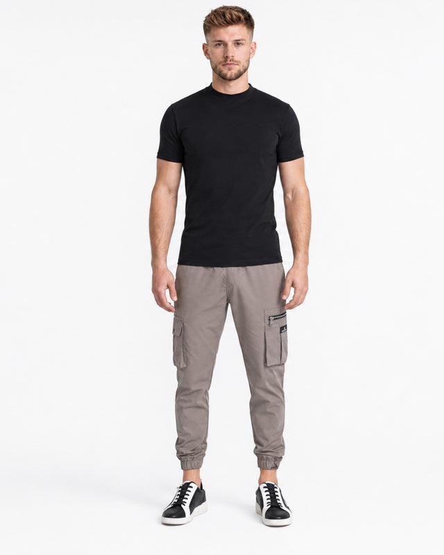 A man stands confidently in a fitted black t-shirt paired with gray cargo pants and stylish sneakers.