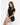 A woman sits elegantly in a fitted black dress with a high neckline and a stylish cutout on one shoulder.