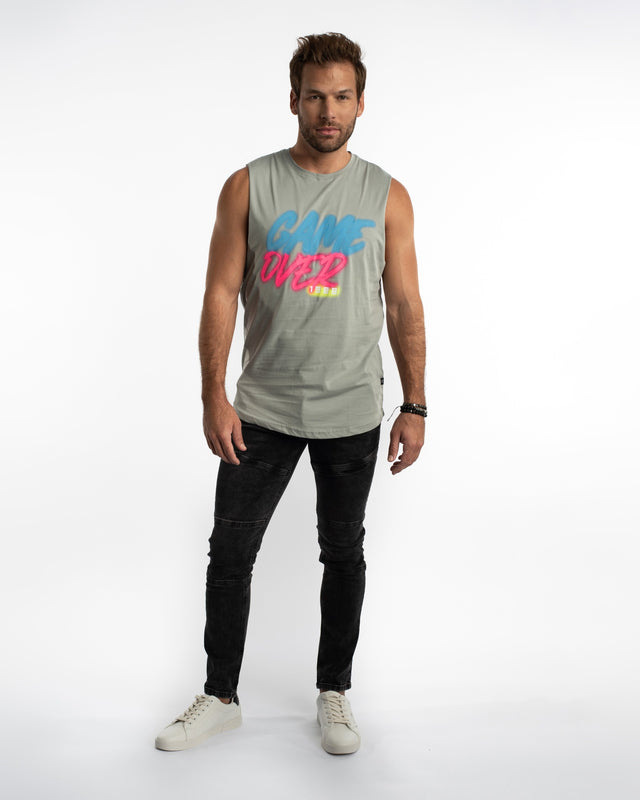 A man wearing a sleeveless light gray top with colorful text, paired with black jeans and white sneakers.