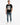 A man stands confidently in a black t-shirt featuring a reflective square design, paired with blue jeans and white sn...