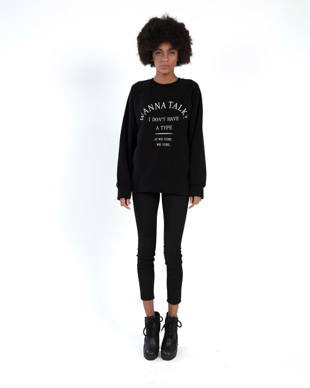 Model wearing Carbon Talk Top black oversized sweatshirt with white graphic text, skinny jeans, and black boots.