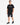 A man stands confidently in a black t-shirt paired with distressed denim shorts and stylish sneakers.