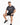 A man sits on a white stool wearing a dark gray t-shirt and black shorts, paired with stylish sneakers.