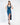A model poses in a deep blue satin dress with a plunging neckline and a thigh-high slit, paired with black heels.