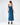 A woman in a sleek, satin blue dress with a fitted silhouette and adjustable straps, viewed from the back.