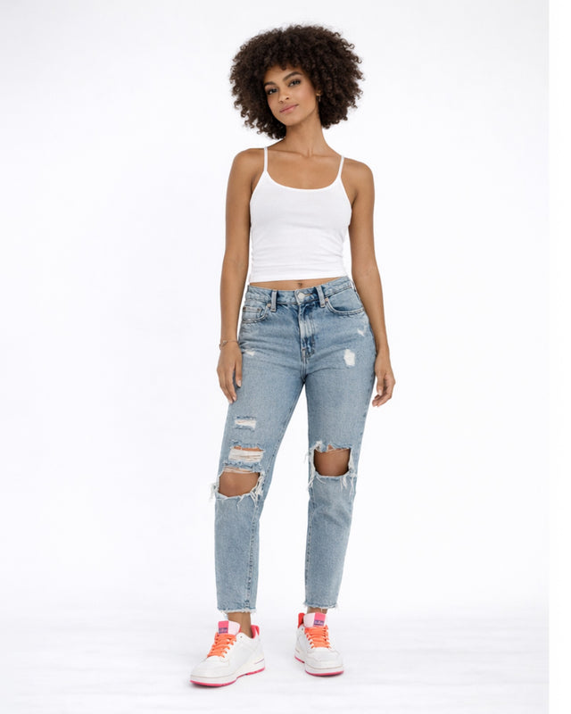 A model poses in a white tank top, distressed light blue jeans, and colorful sneakers against a plain background.