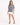 A model poses in a gray tie-dye tee featuring playful hand graphics, paired with a white skirt and black heels.