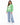 A woman stands wearing a green sweatshirt with a graphic design, paired with light blue wide-leg jeans and white snea...