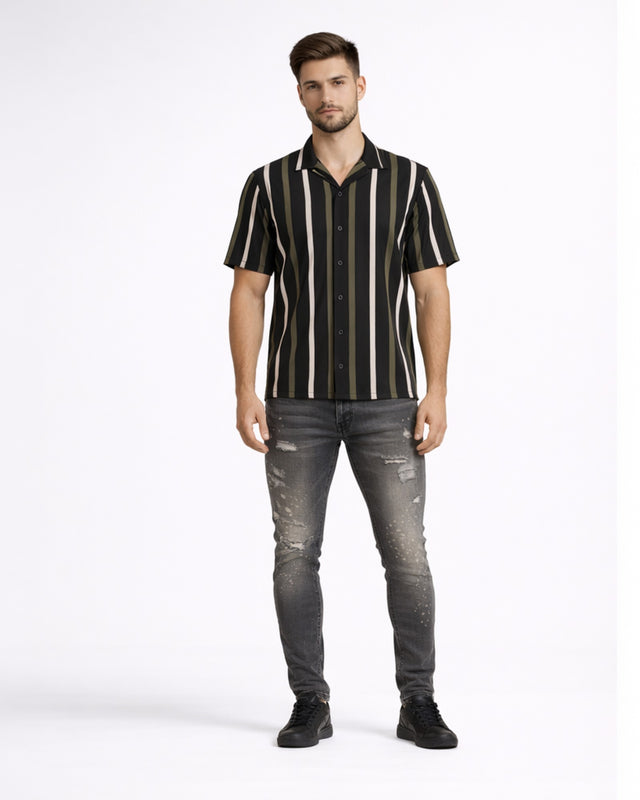 A man stands wearing a short-sleeve striped shirt with dark and light vertical lines, paired with distressed jeans.