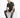 A man sits on a white cube, wearing a short-sleeve striped shirt with dark and light tones, paired with distressed je...
