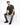 A man sits on a white cube, wearing a short-sleeve striped shirt with dark and light tones, paired with distressed je...