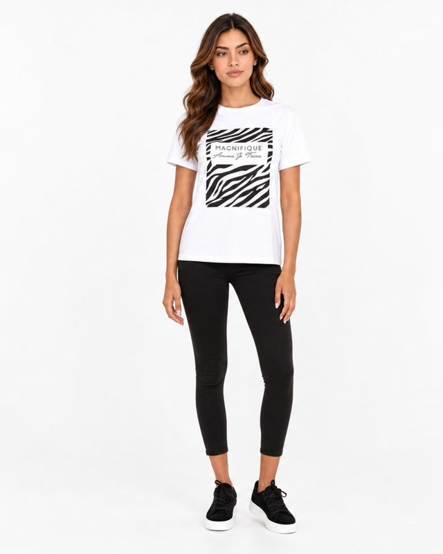 A woman stands wearing a white t-shirt with a zebra print graphic, paired with black leggings and sneakers.