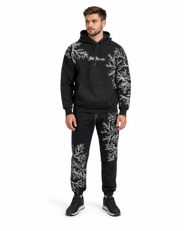A man wearing a black hoodie and matching sweatpants with a unique coral-like design in gray.