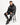 A man sits on a stool wearing a black hoodie and matching sweatpants with a coral-inspired design.
