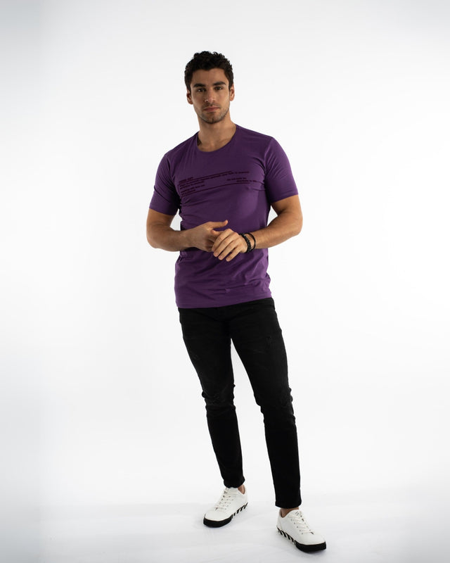 A man stands confidently in a purple short-sleeve shirt and black jeans, wearing white sneakers.