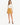 A woman stands confidently in a light blouse with a chain detail and a mustard-colored mini skirt, paired with black...