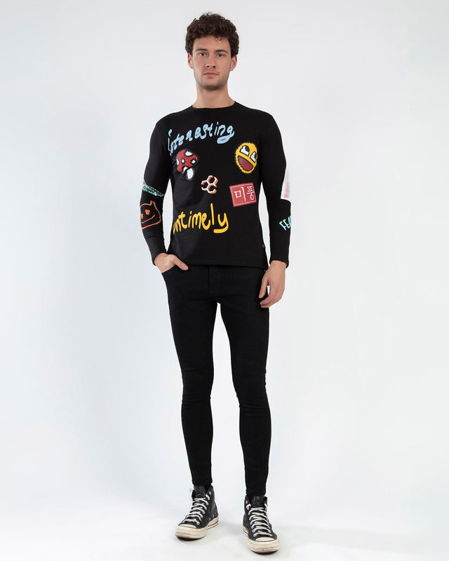 A model wearing a black long-sleeve shirt featuring colorful graphic designs and text, paired with black skinny jeans.