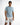 A man stands confidently in a light blue short-sleeve shirt paired with distressed white shorts.