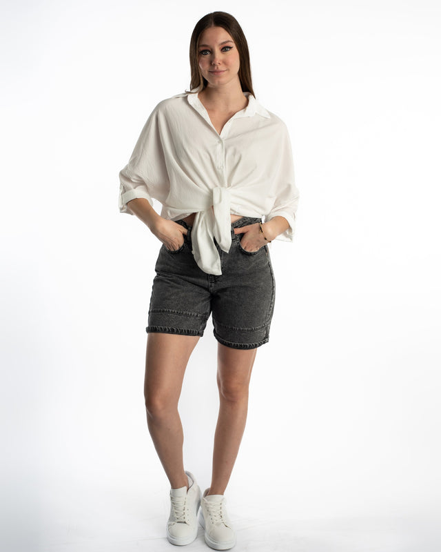 Model in high-waisted Maxine grey washed denim shorts with a white tie-front shirt and sneakers.