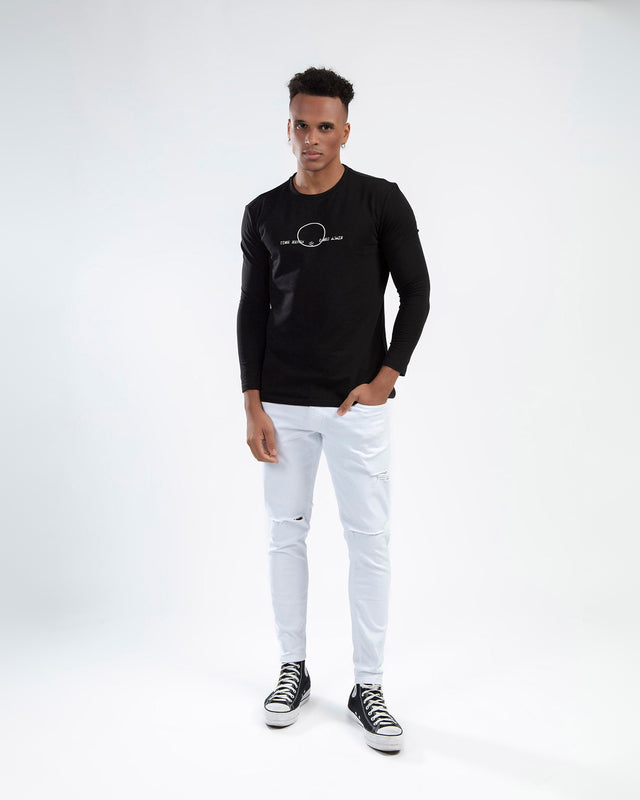 Man in Elliott white distressed jeans with knee rips and urban streetwear styling against a white background.