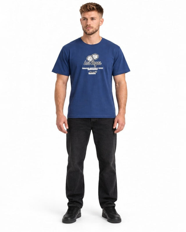 A man stands wearing a blue graphic t-shirt featuring a playful design and casual black jeans.