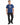 A man stands wearing a blue graphic t-shirt featuring a playful design and text, paired with black jeans and sneakers.
